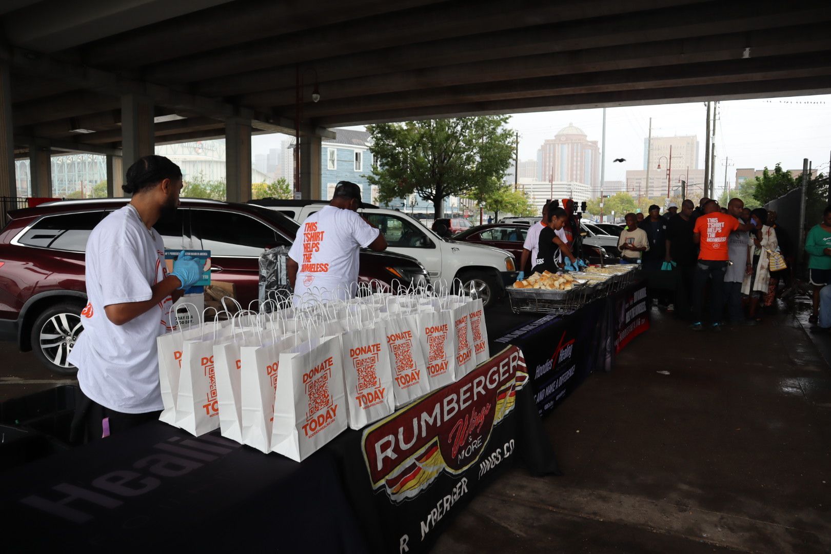 A group of people are standing around a table with rumberger 's hot dogs on it.