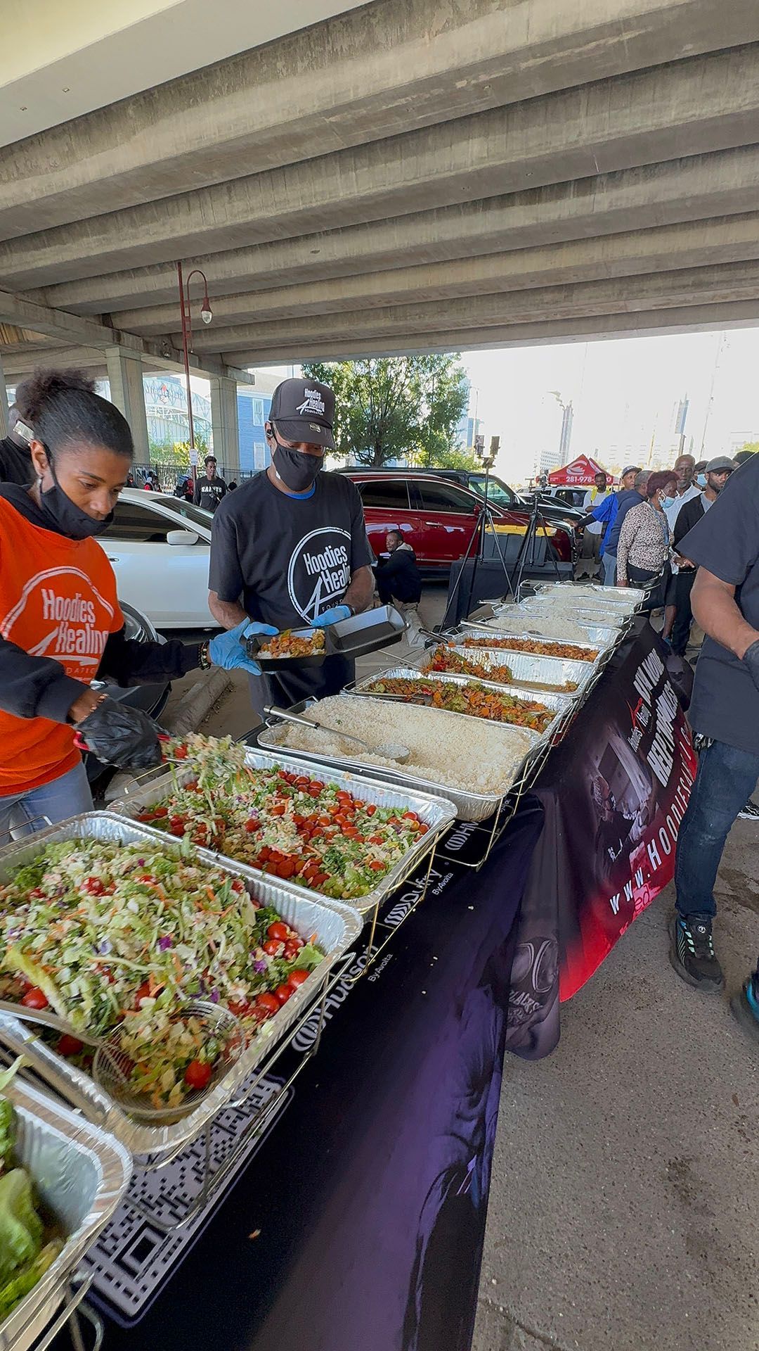 A group of people are standing around a table filled with plates of food.