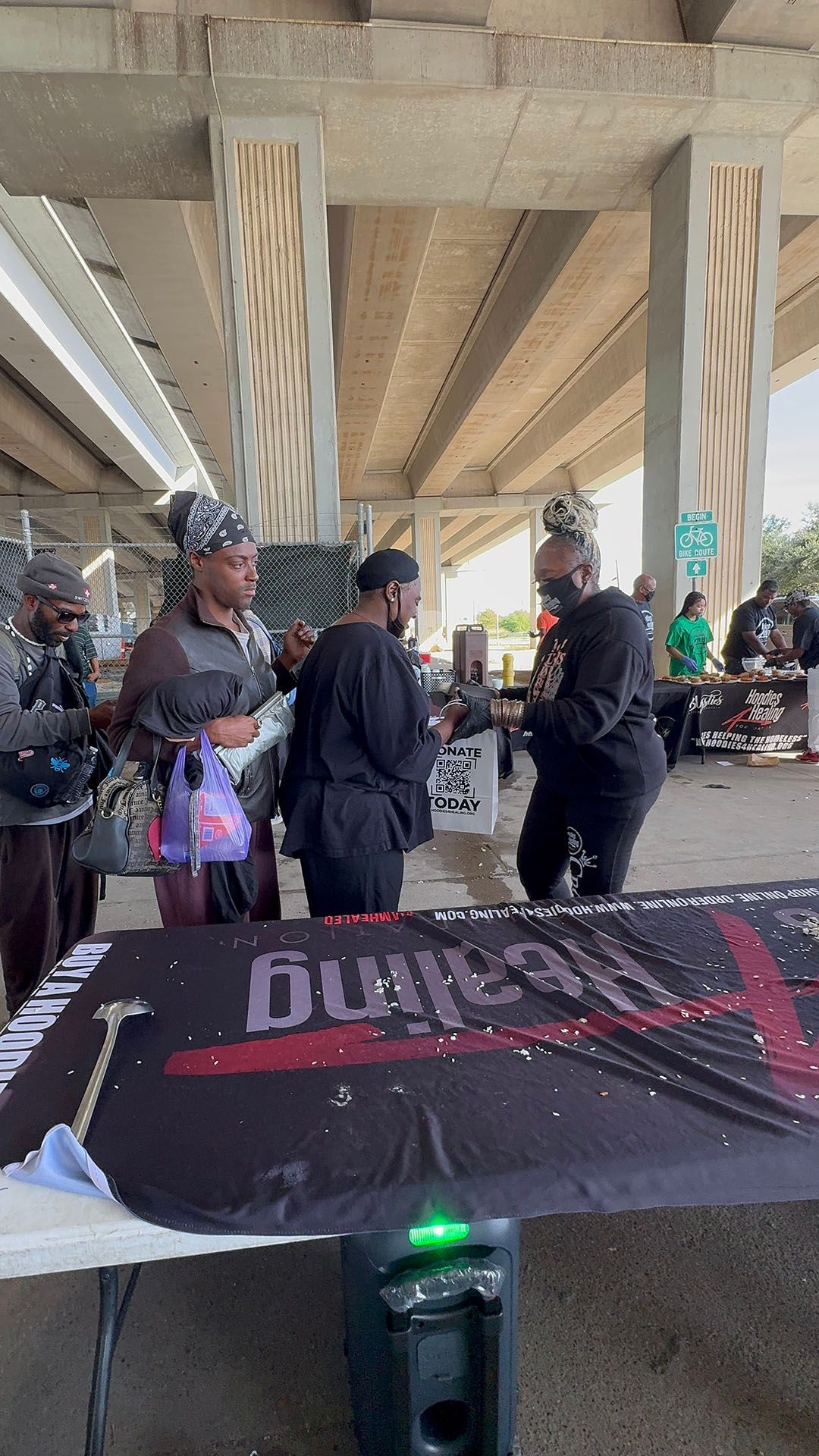 A group of people are standing around a table under a bridge.