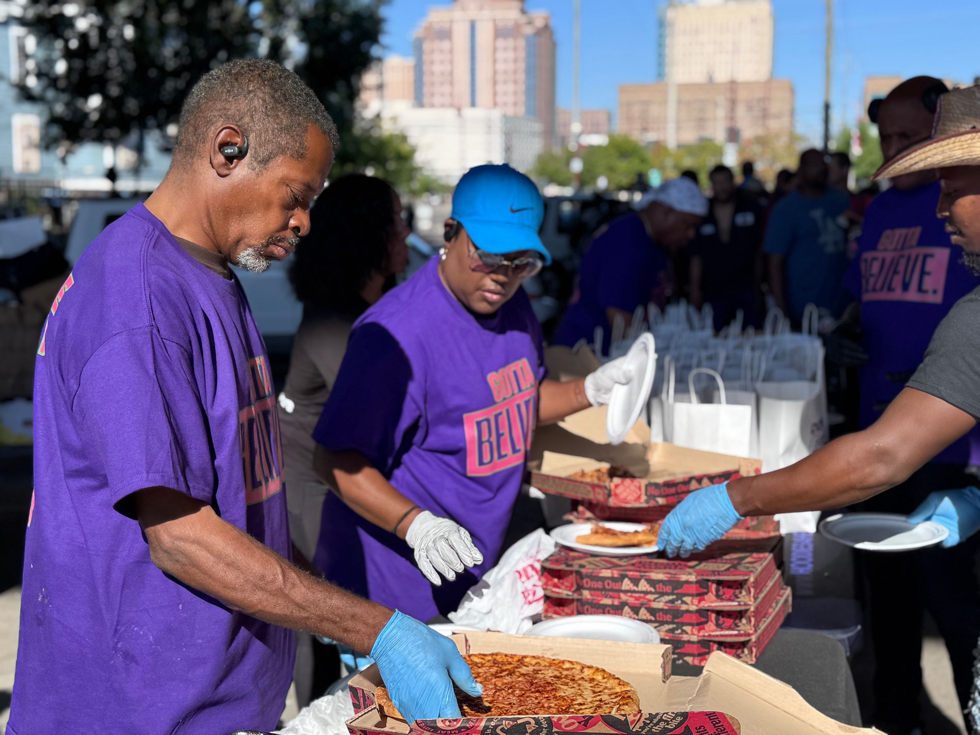 A group of people in purple shirts are serving pizza