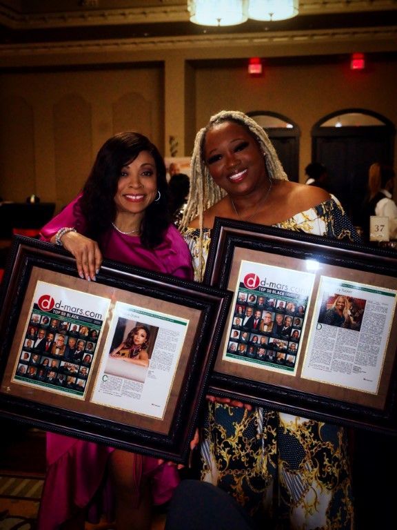 Two women are posing for a picture while holding framed pictures