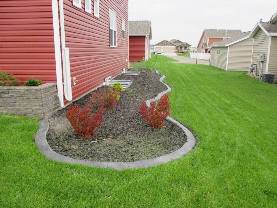 Red siding with a landscaped bed bordered by concrete, green grass.