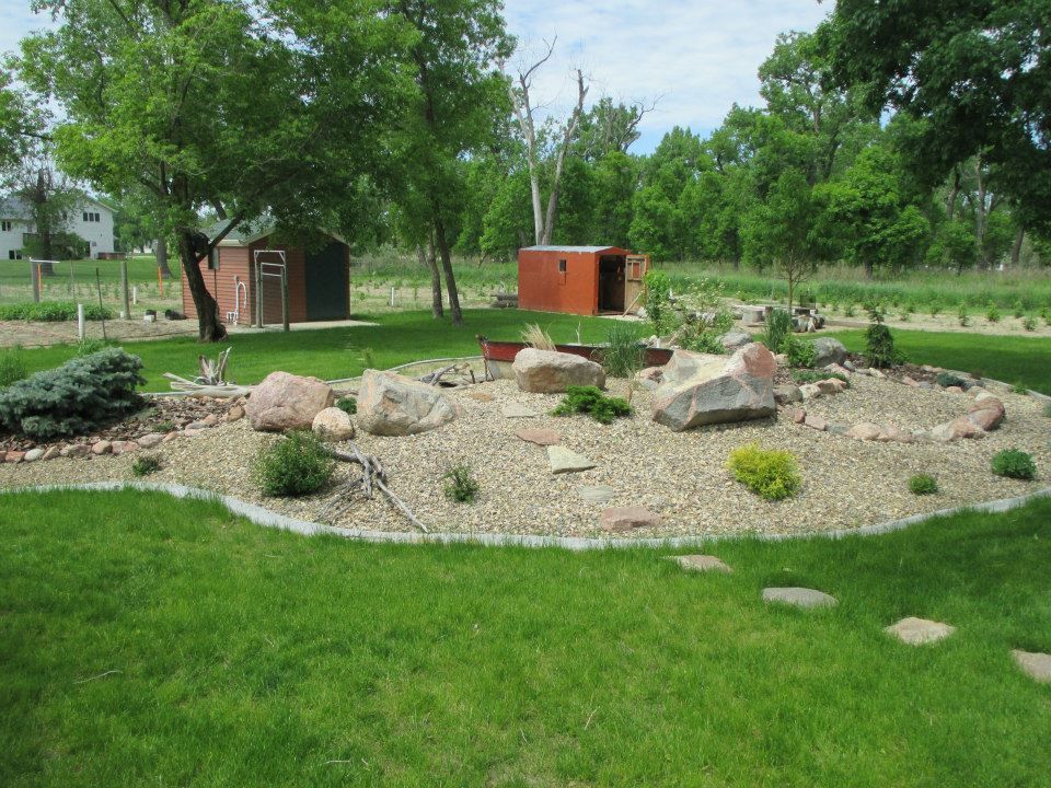 A landscaped yard with a rock garden, two small sheds, and lush green grass.