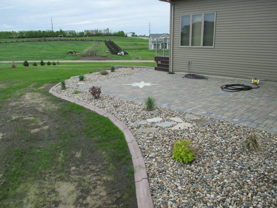 A house with a stone patio and garden bed.  Green grass in the foreground.