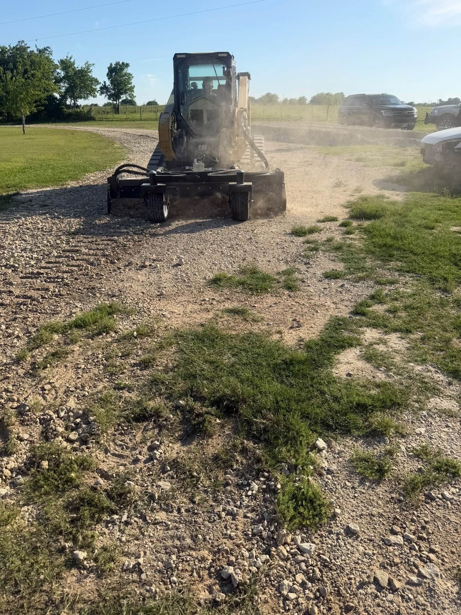 Tractor mowing a gravel field, kicking up dust on a sunny day.