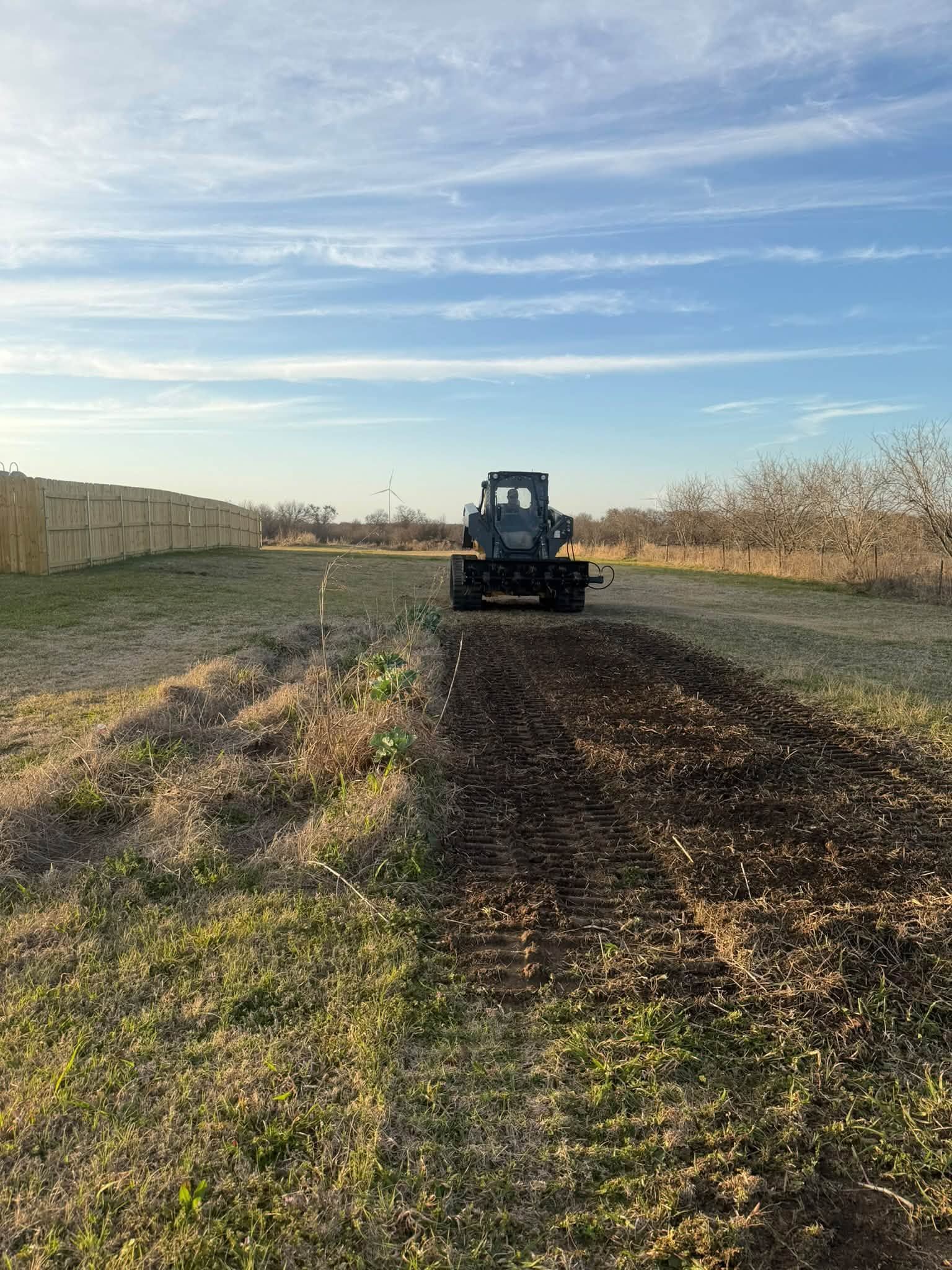 Small tractor driving on a muddy field under a bright blue sky.
