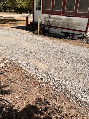 Gravel driveway beside a weathered red-and-white house with a small utility pole.