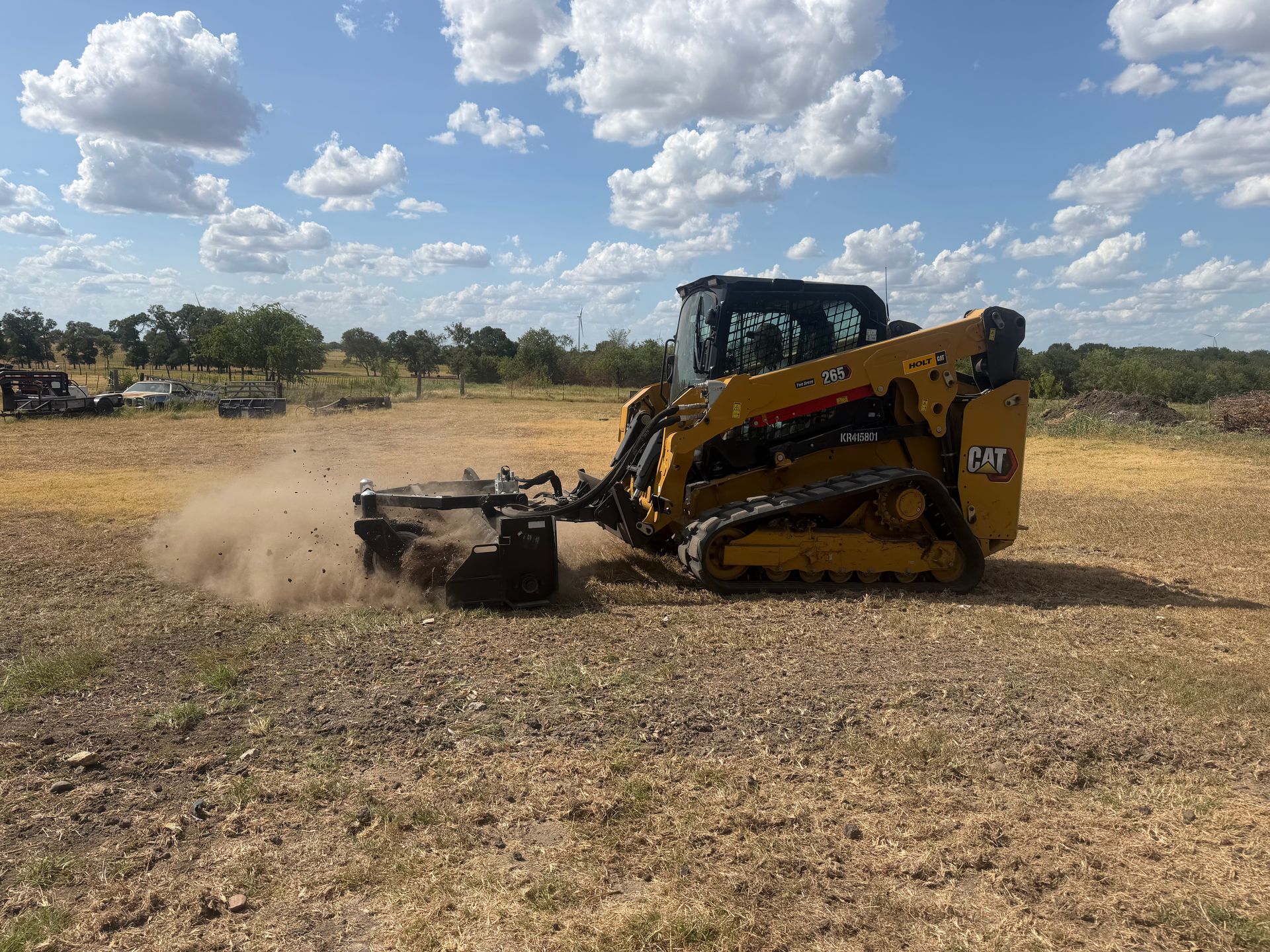 Yellow CAT bulldozer kicking up dust on a dry field under a cloudy sky
