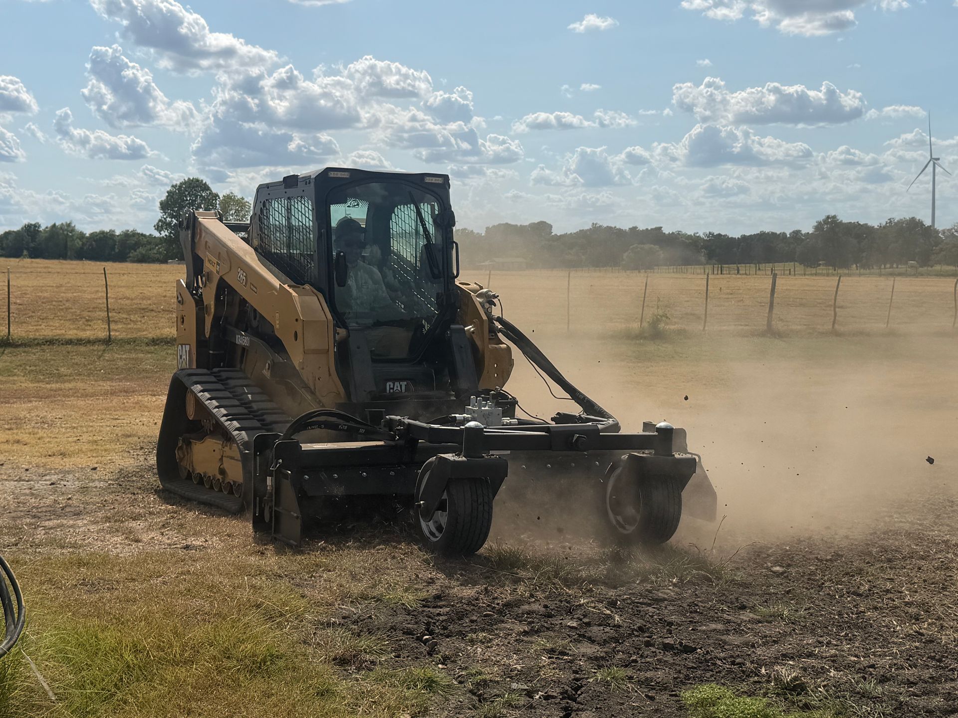 Yellow skid steer clearing dusty ground in a field under a blue sky