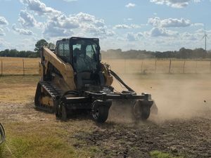 Yellow skid steer clearing dirt in a dusty field under a blue sky