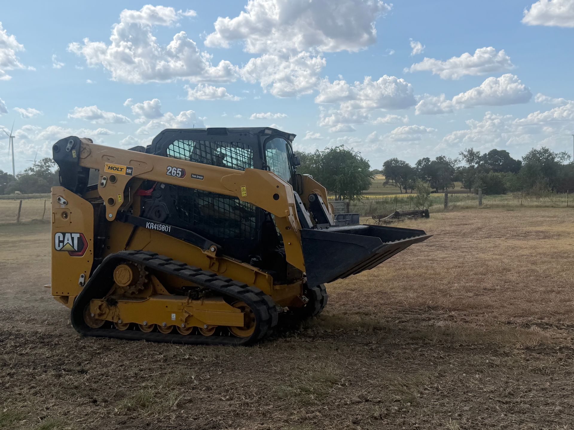 Yellow CAT compact track loader in a dry field under a cloudy sky