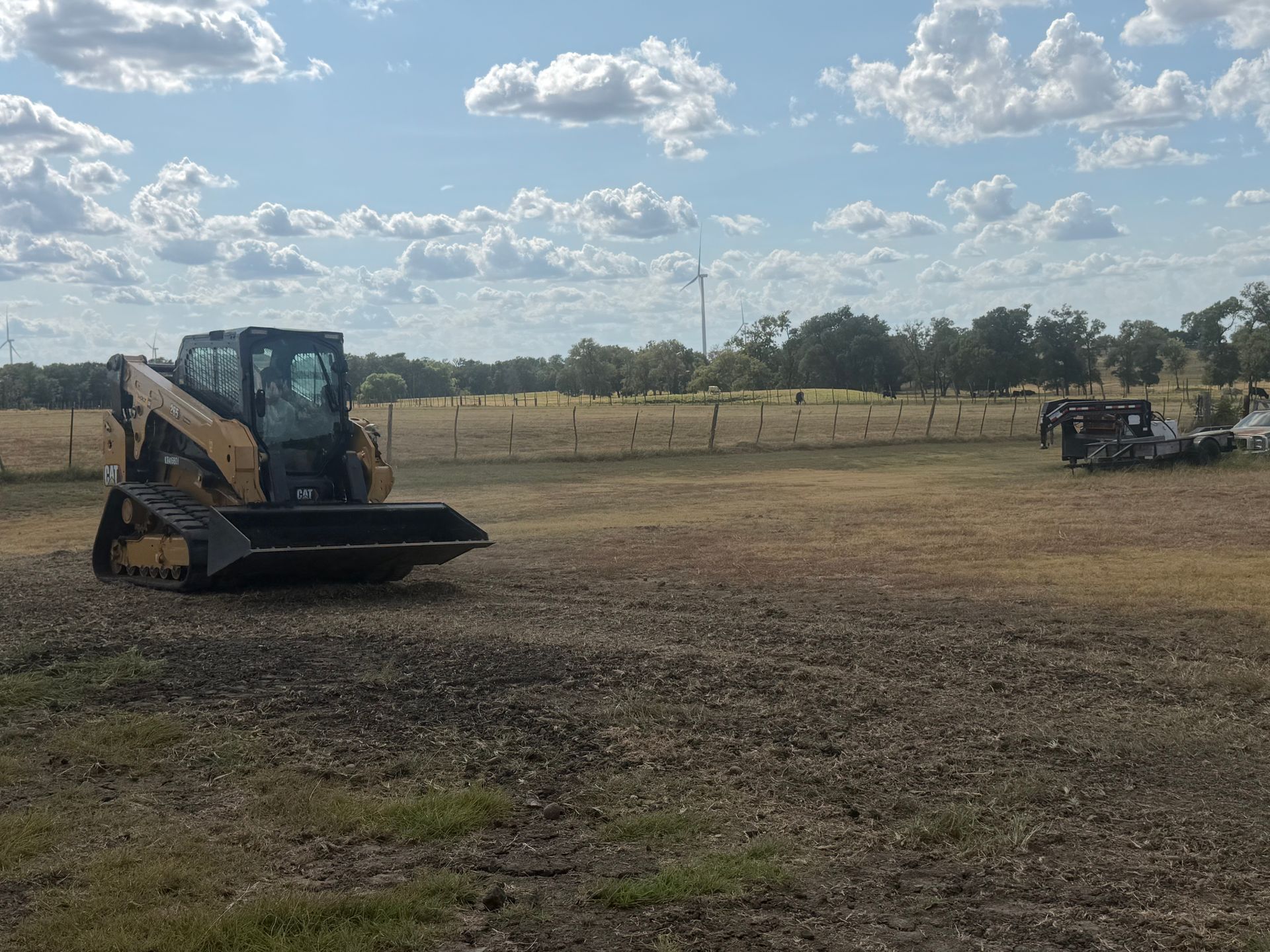 Yellow skid-steer loader on a dirt field under a cloudy sky.