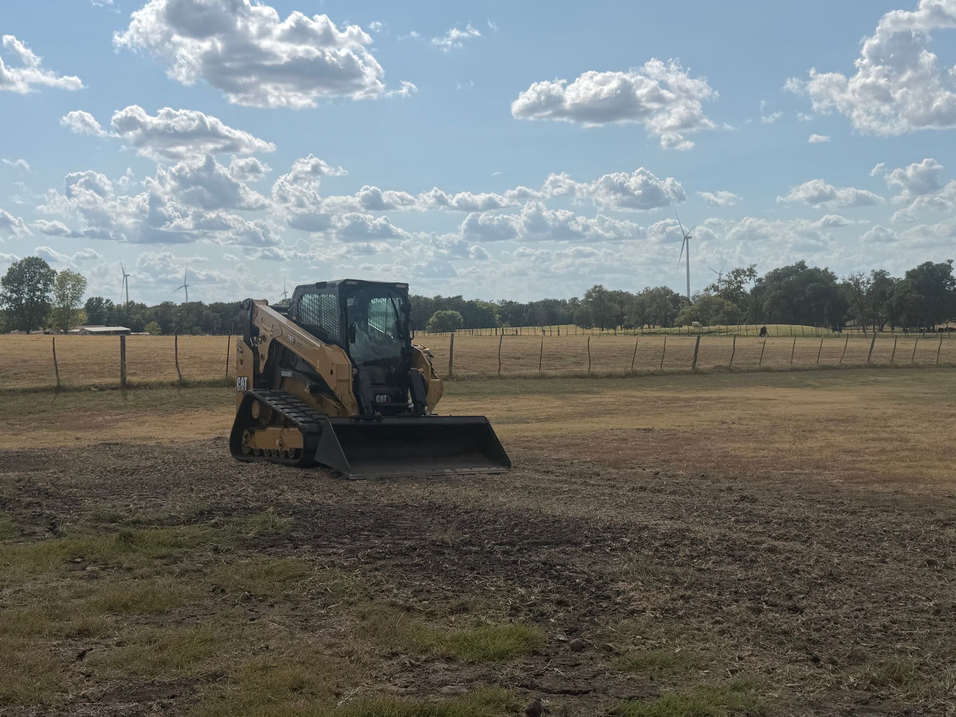 Yellow skid steer on a dirt field under a partly cloudy sky