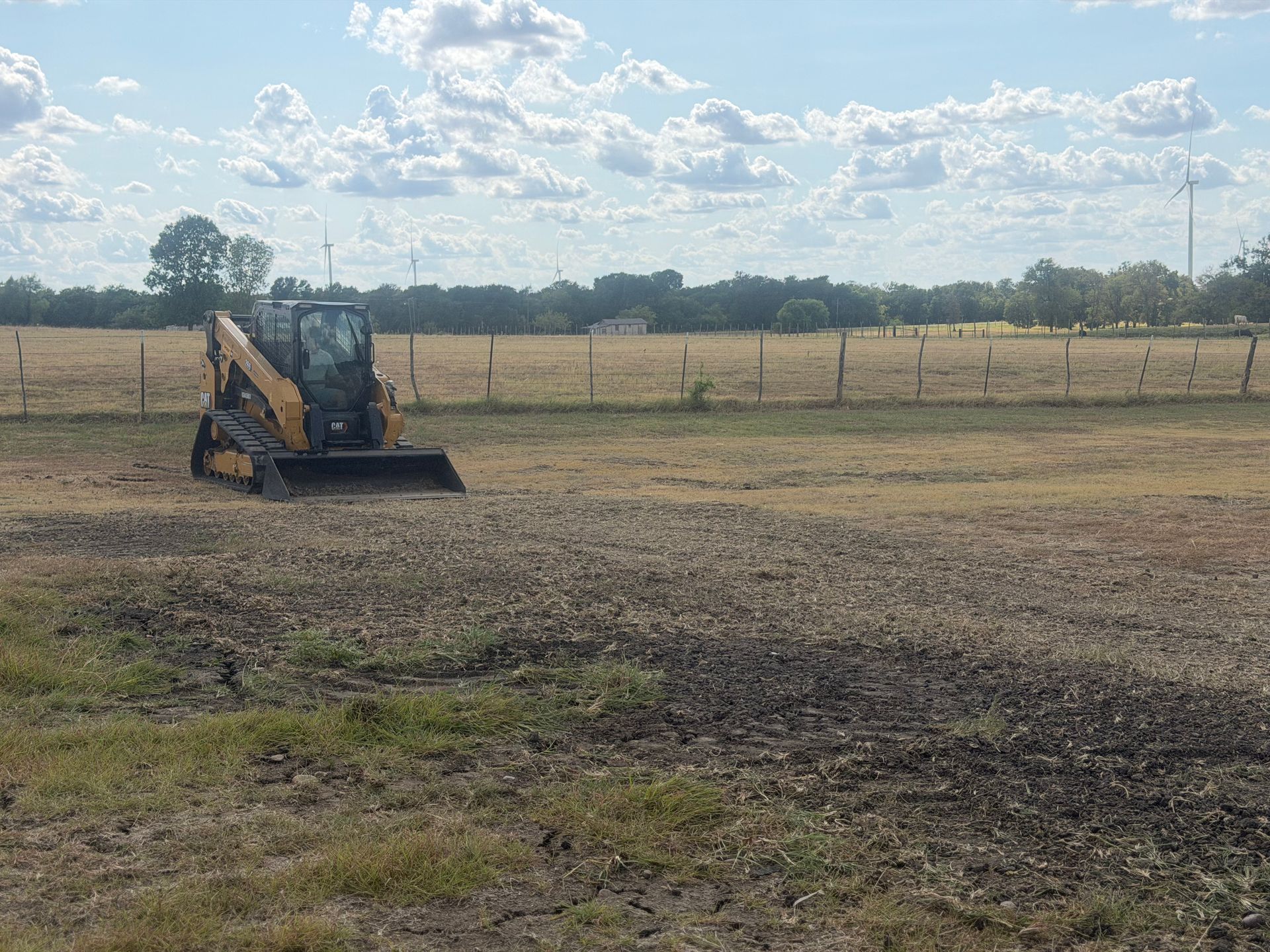 Yellow backhoe on a dry, open field under a partly cloudy sky