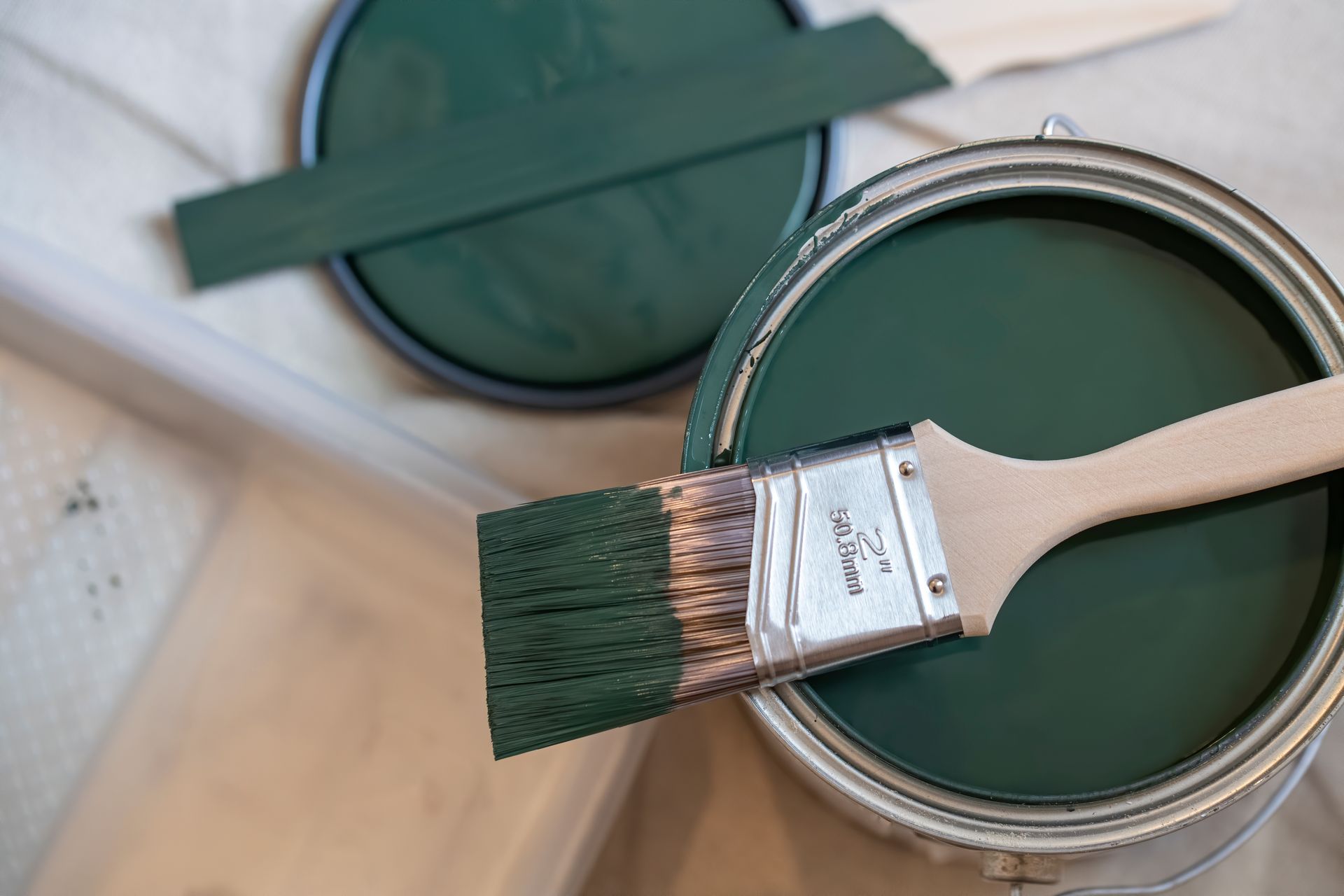 Open paint can with green paint, paintbrush, and paint can lid.