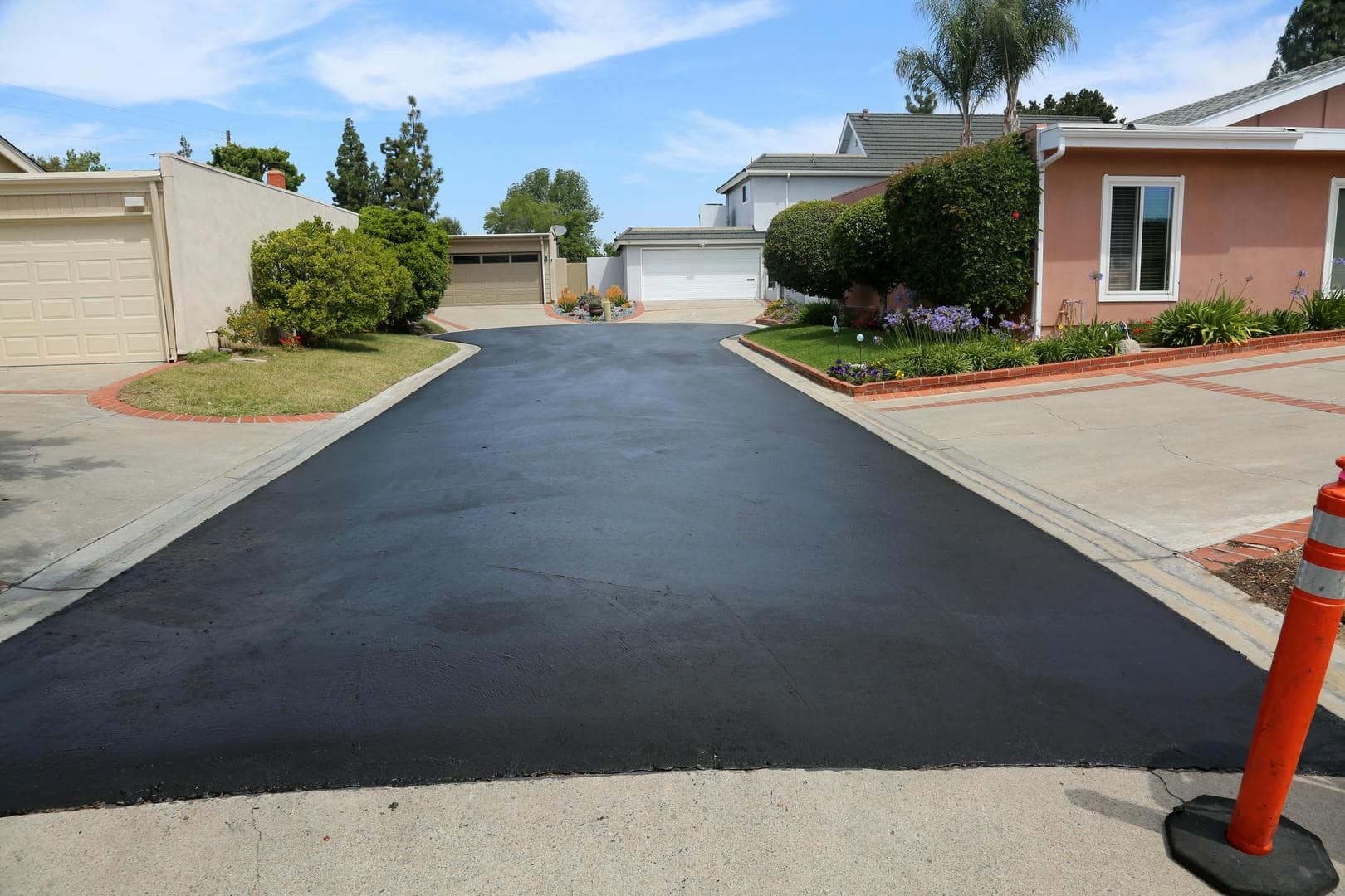 Newly paved asphalt driveway in front of houses; orange traffic cone on right.