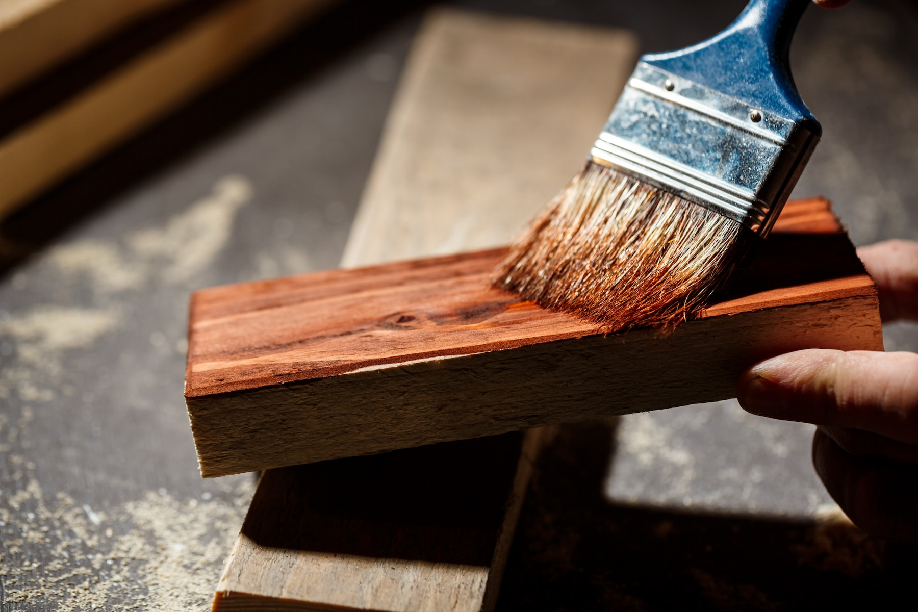 Hand applying stain to a wooden block with a brush, close-up.