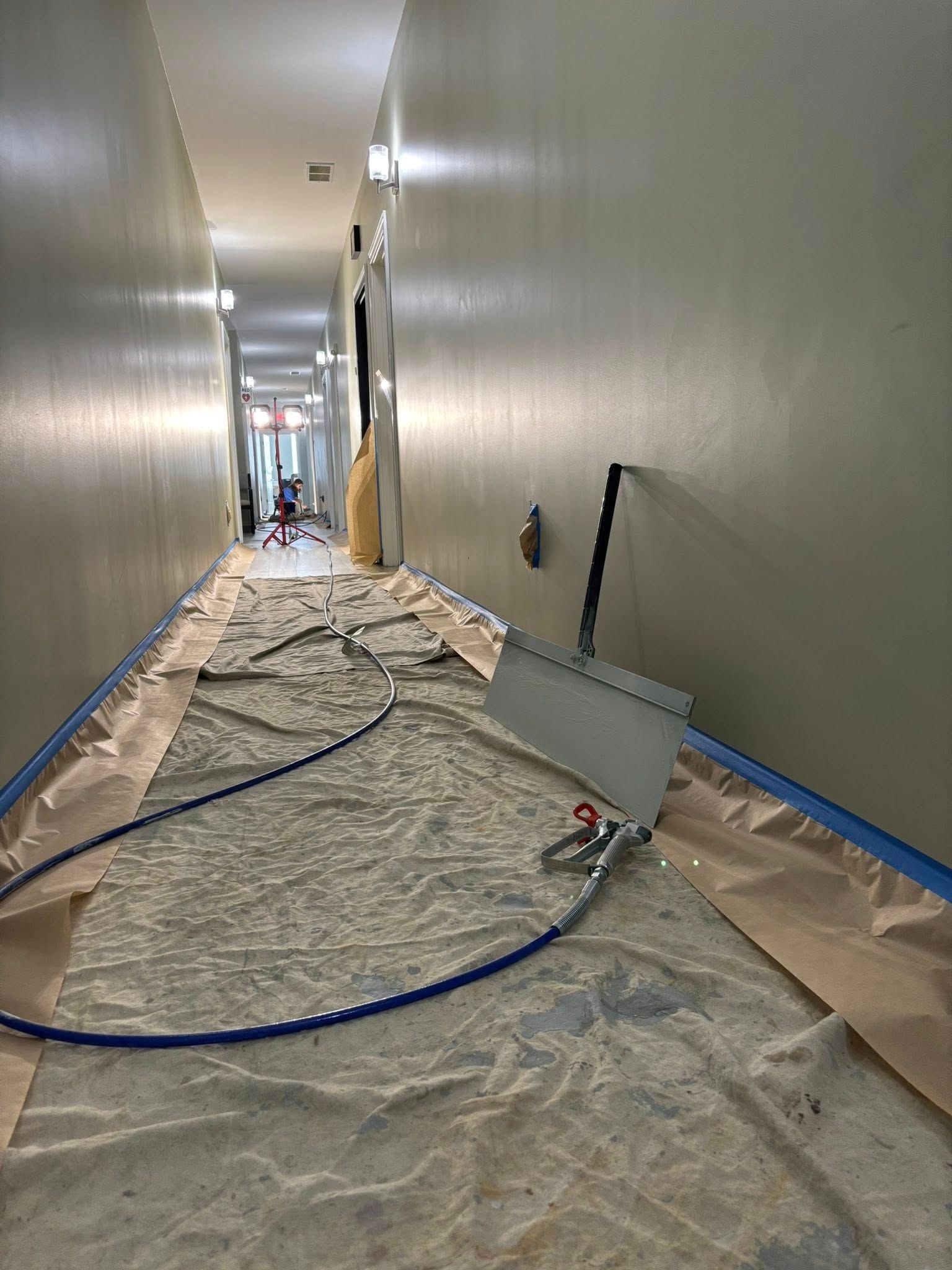 Hallway during painting project, covered floor, equipment present. Walls are painted.