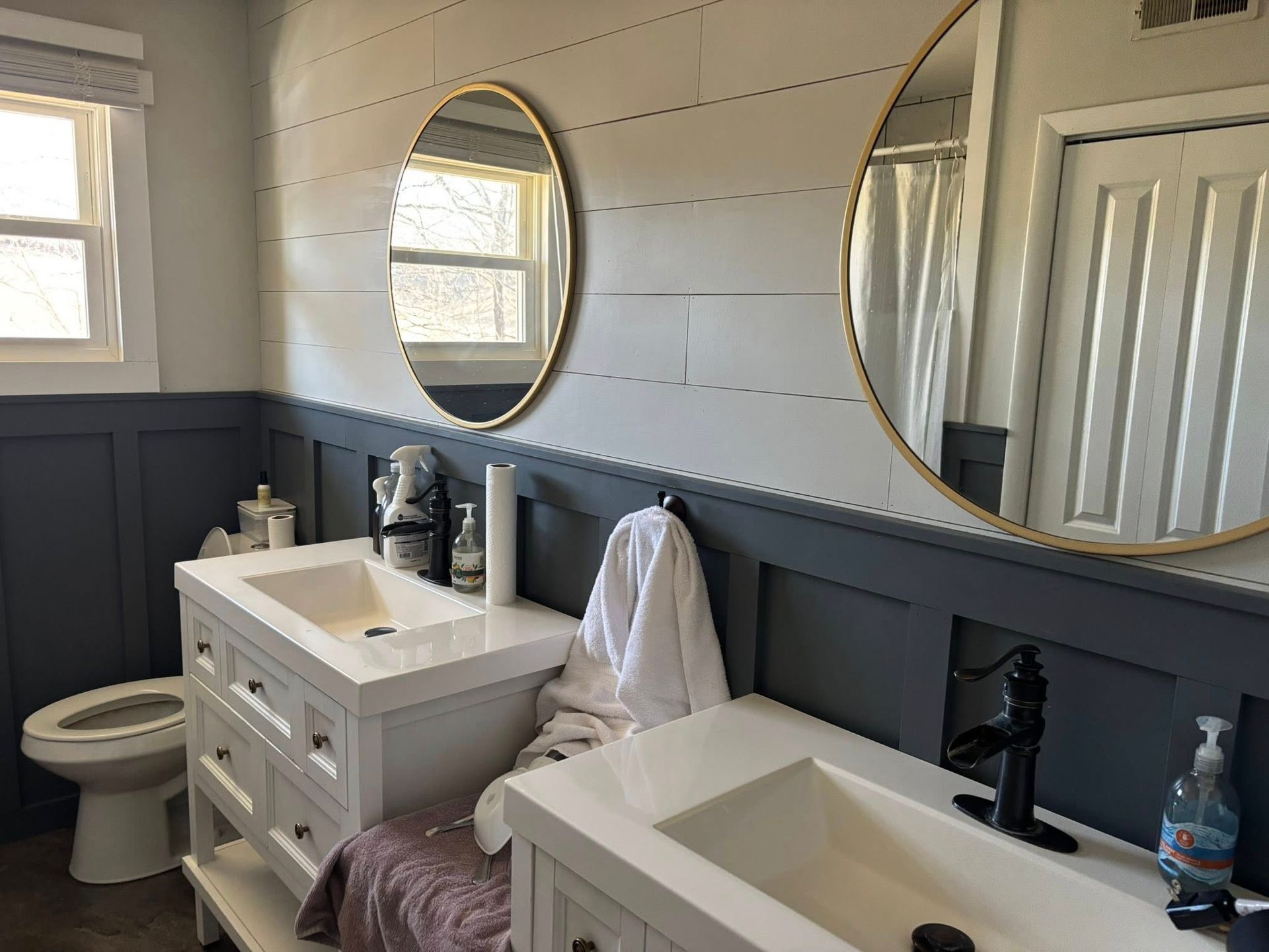 Bathroom with white double vanity, blue accent wall, round gold-framed mirrors, and a window.
