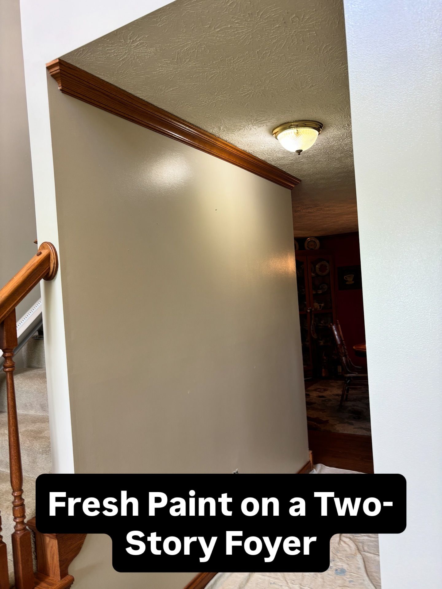 Freshly painted two-story foyer wall, tan color, with wooden trim and staircase visible.
