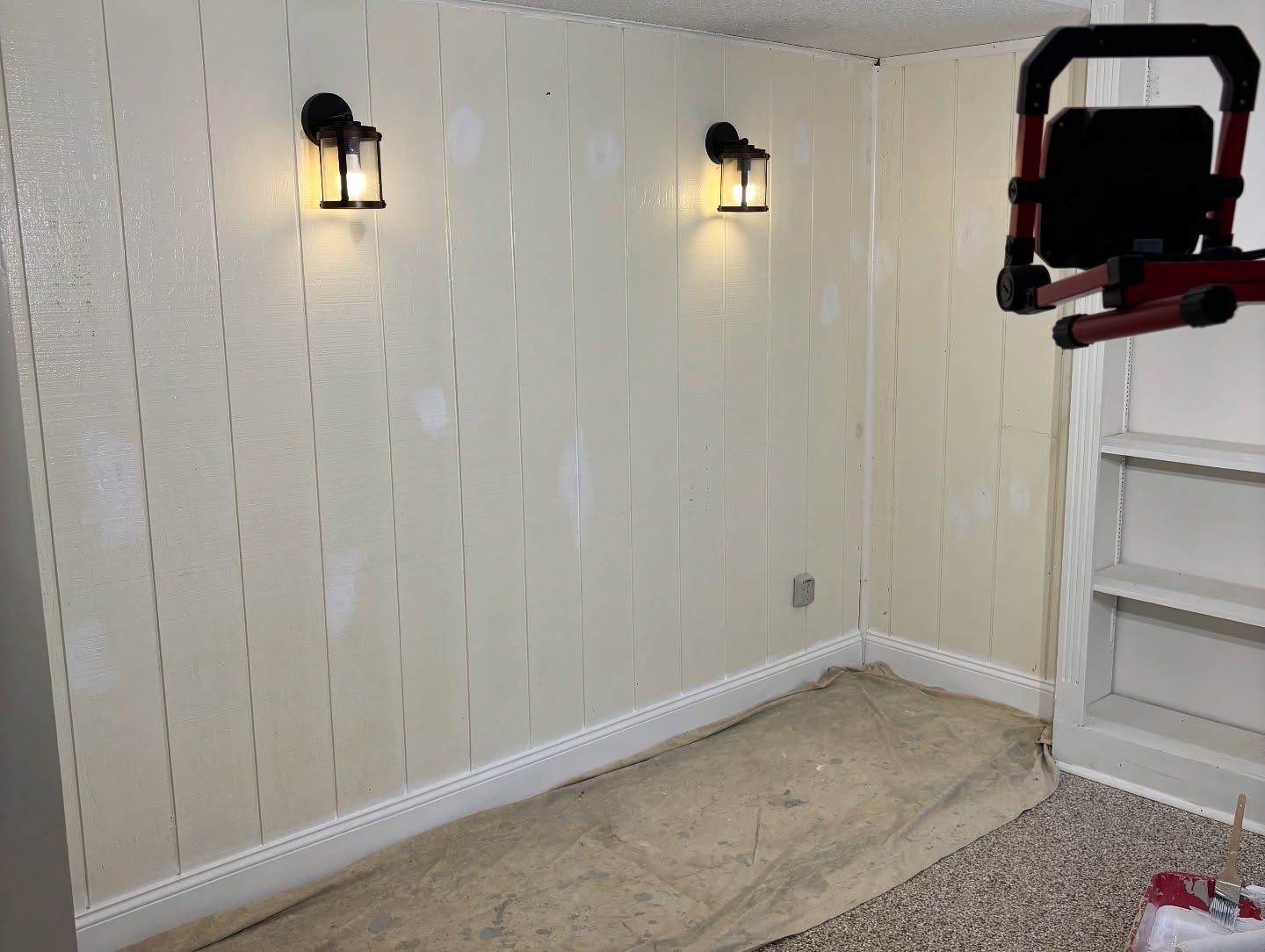 Cream-colored paneled walls with two sconces. A work light and built-in shelving are also visible in the corner of a room.
