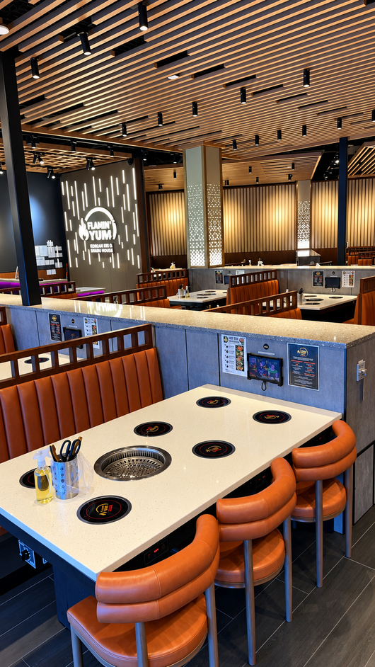 Modern restaurant interior with tables, orange stools, booths, and a patterned ceiling
