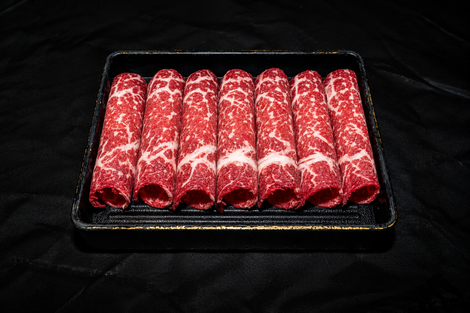 Five red patterned rolled items arranged in a black tray on a dark background