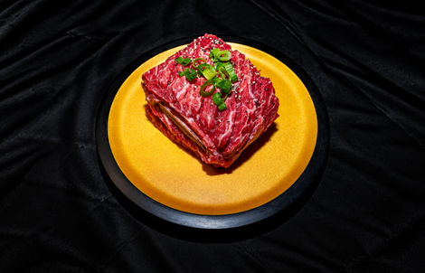 Raw marbled steak topped with herbs on a yellow plate against a black background