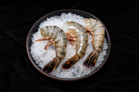 Three raw shrimp on crushed ice in a dark bowl