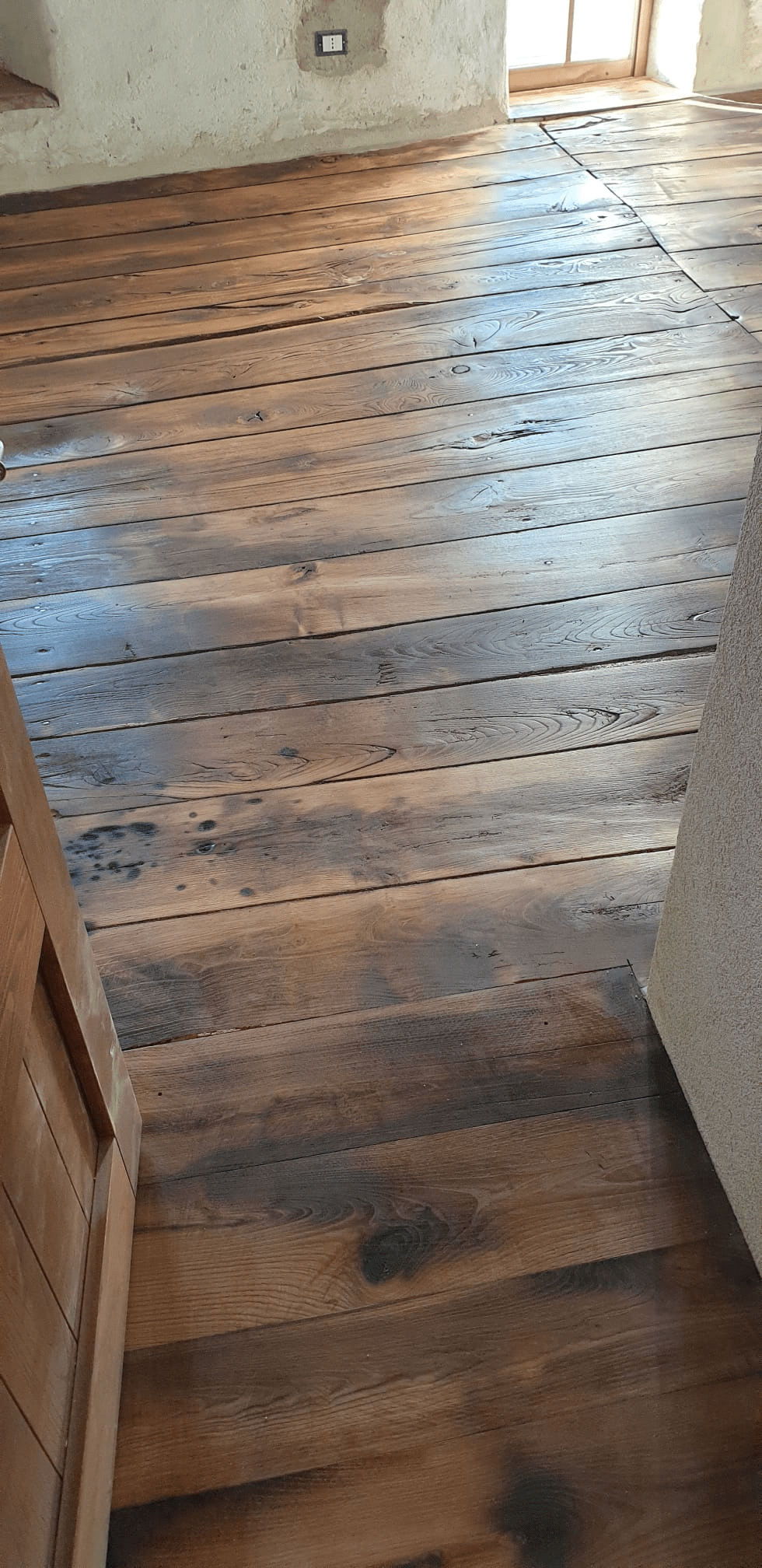 Pavimento in assi di legno in una stanza con pareti chiare e una porta parzialmente visibile.