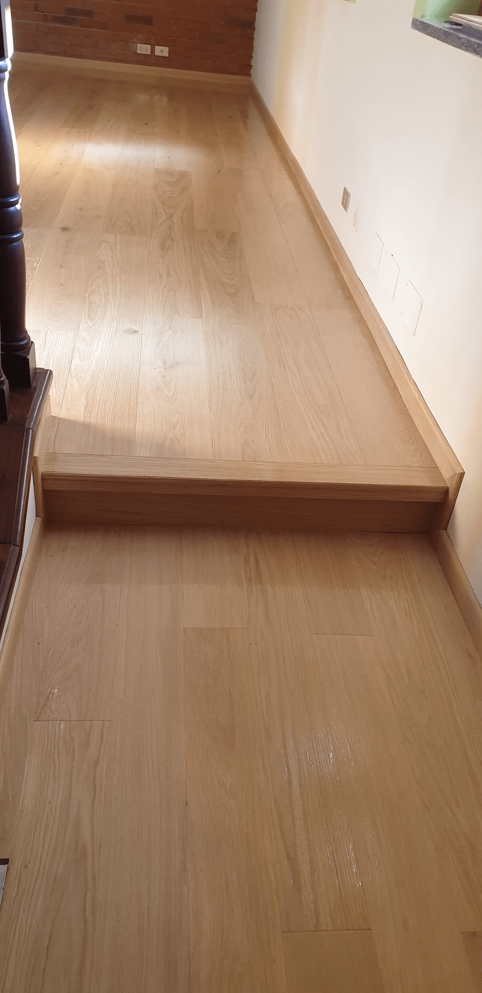 Pavimento in legno con un gradino, accanto a una parete bianca.