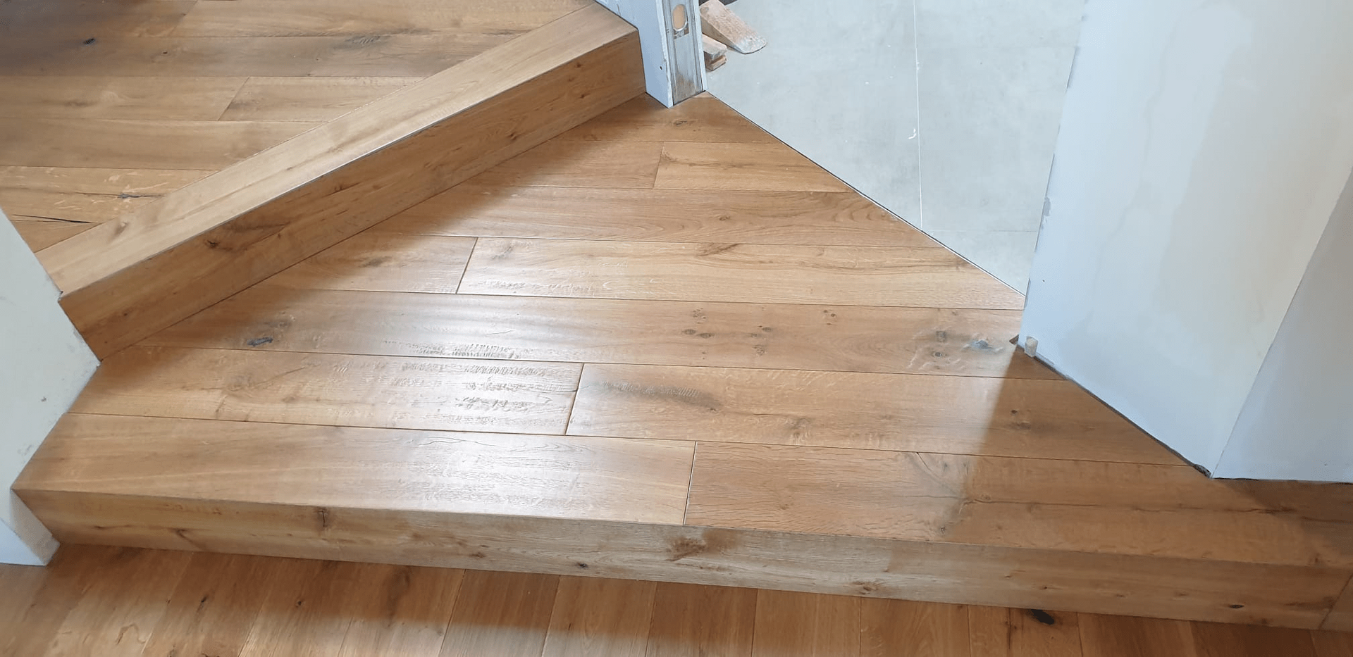 Scala in legno con pavimento in legno marrone chiaro e pareti bianche.