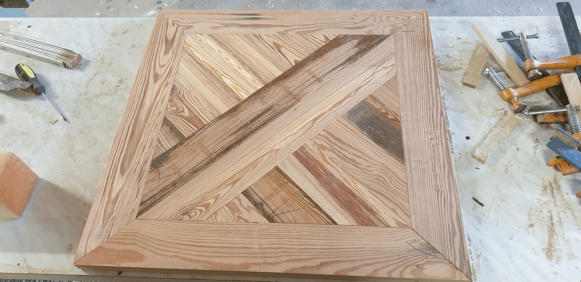 Piano del tavolo in legno con motivo a spina di pesce intarsiato; utensili per la lavorazione del legno nelle vicinanze.