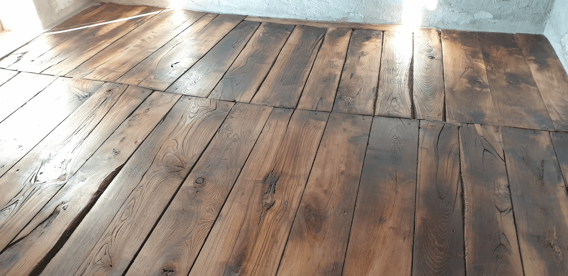 Pavimento in legno con diverse tonalità di marrone e venature del legno visibili, illuminato dalla luce naturale.