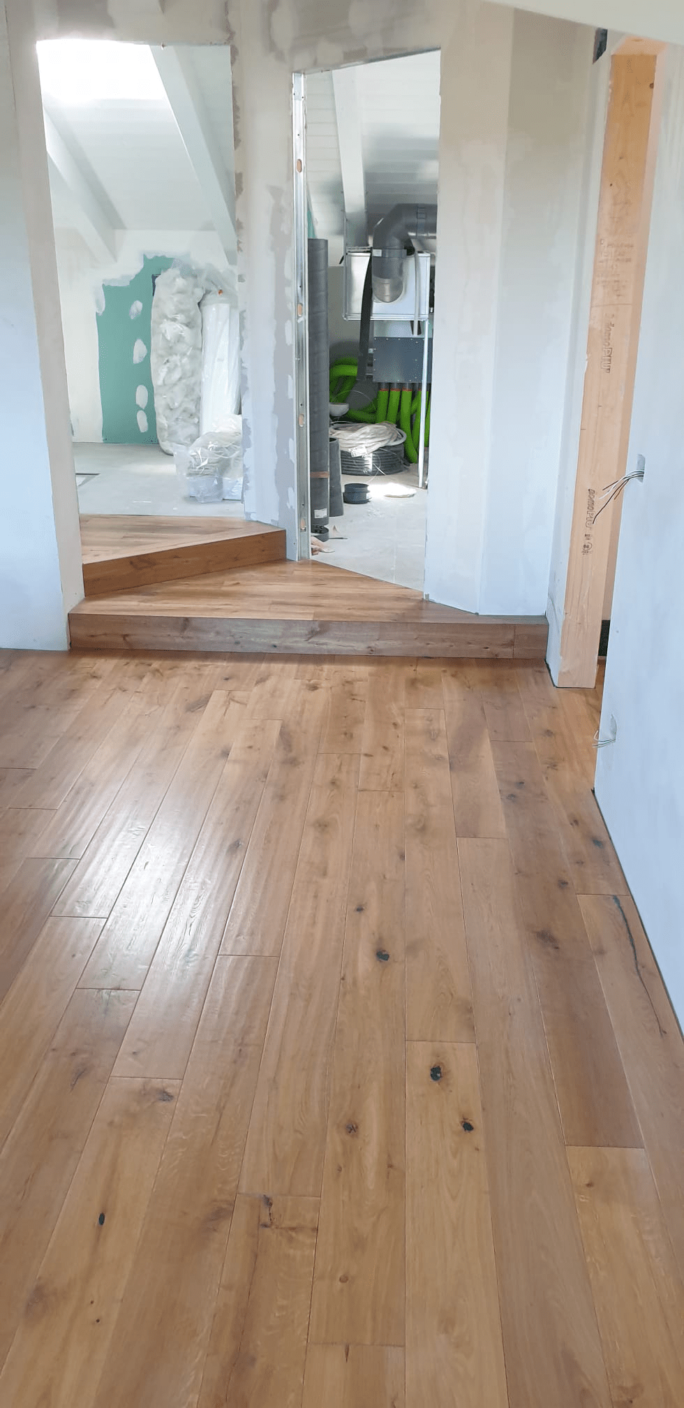 Il pavimento in legno e le scale conducono a una porta aperta, che rivela una stanza parzialmente costruita.
