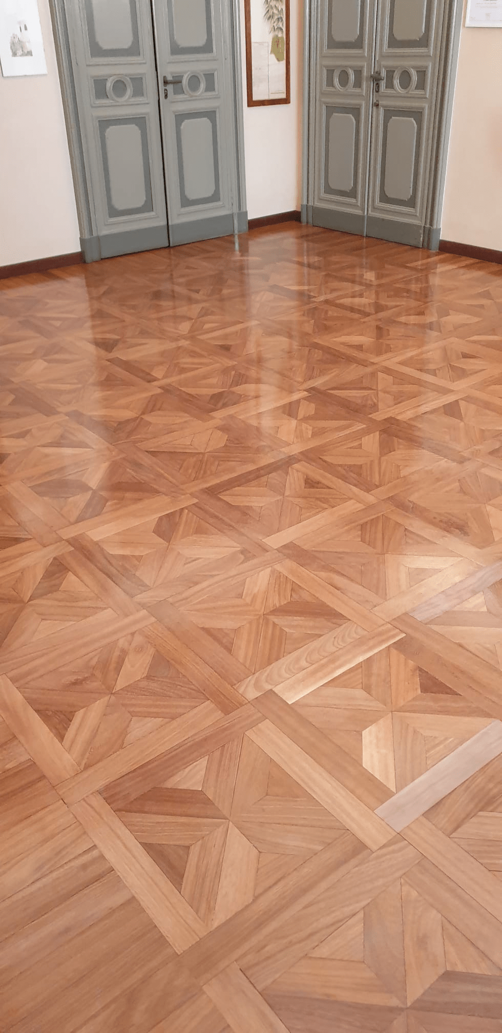 Pavimento in parquet in una stanza con due porte grigie. Il pavimento presenta un motivo geometrico.