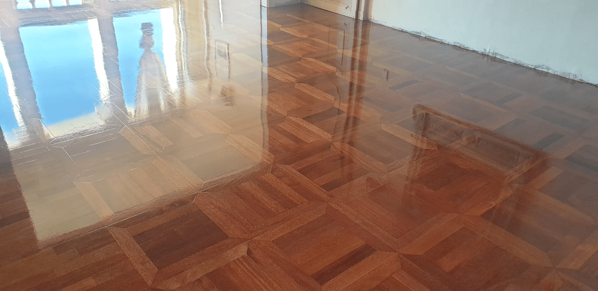 Pavimento in legno laccato lucido che riflette una finestra e i dettagli della stanza. Tavole marroni in stile parquet.