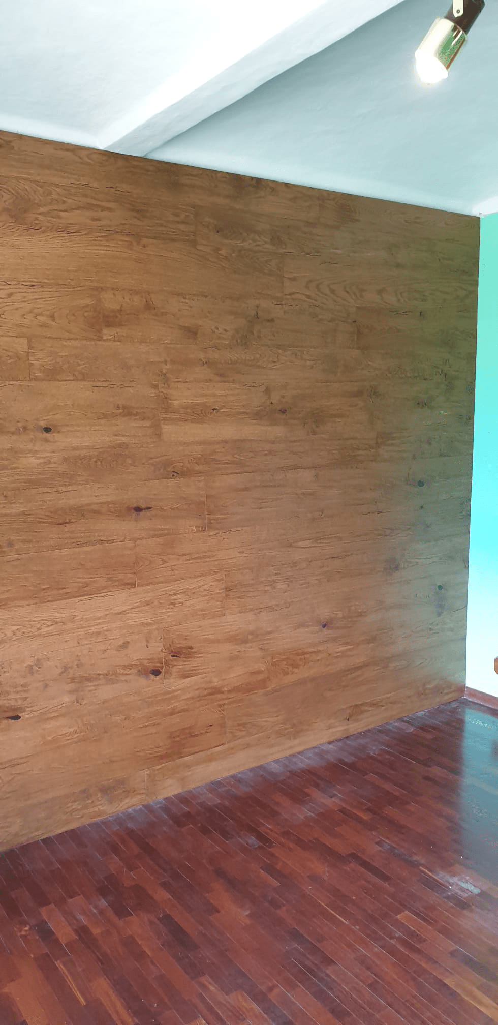 Una stanza con una parete decorativa in legno e pavimento in legno. Un soffitto con lampada e una parete turchese.