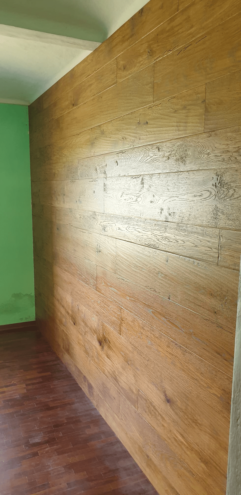 Parete in legno in una stanza, con linee orizzontali visibili. Parete verde e pavimento marrone.