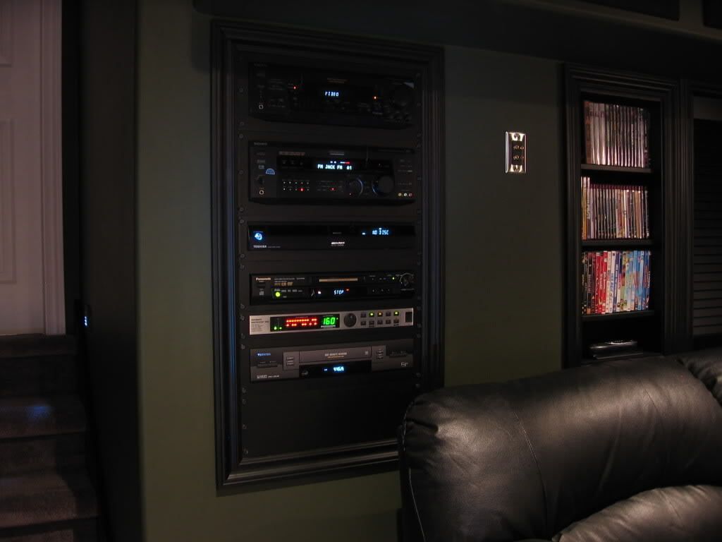 Black audio/video equipment rack built into a green wall, next to a DVD shelf.