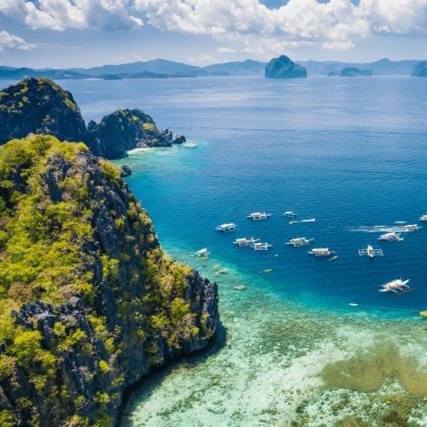 Emerald water and rocky cliffs with boats, El Nido, Philippines.