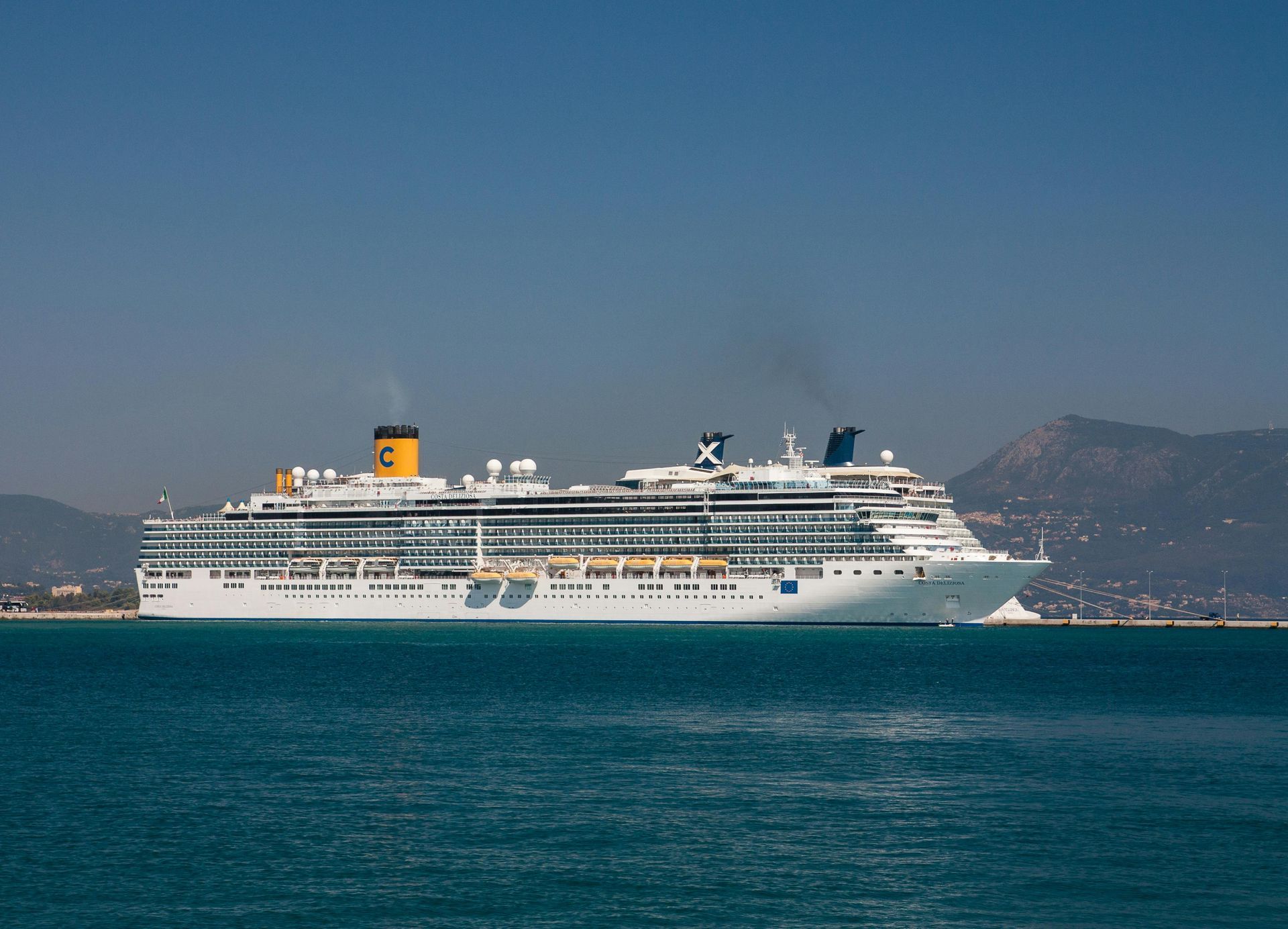 Large white cruise ship on blue water under a clear blue sky.