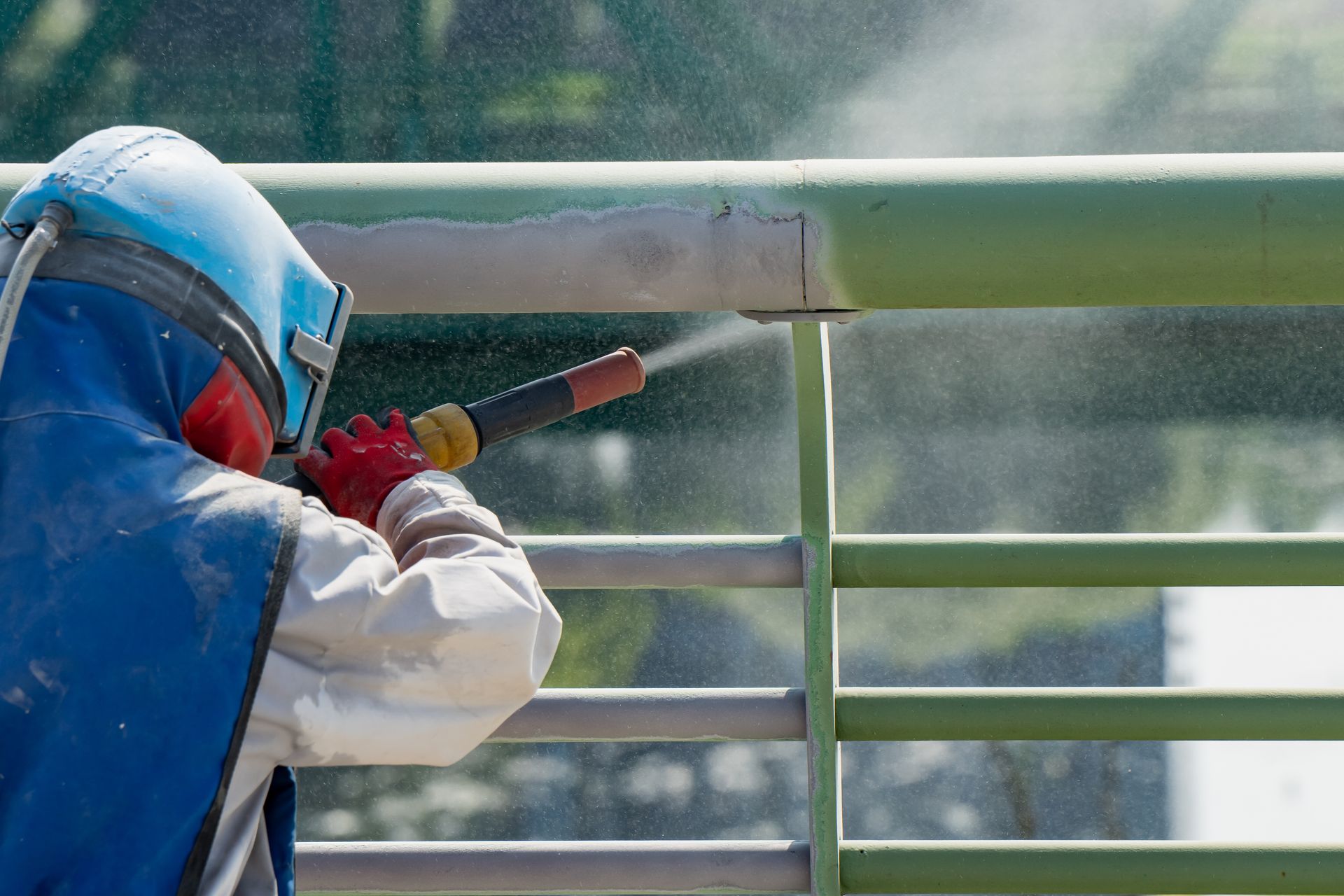 Worker in blast helmet and gloves sandblasting a green metal railing. Worker in blast helmet and gloves sandblasting a green metal railing.