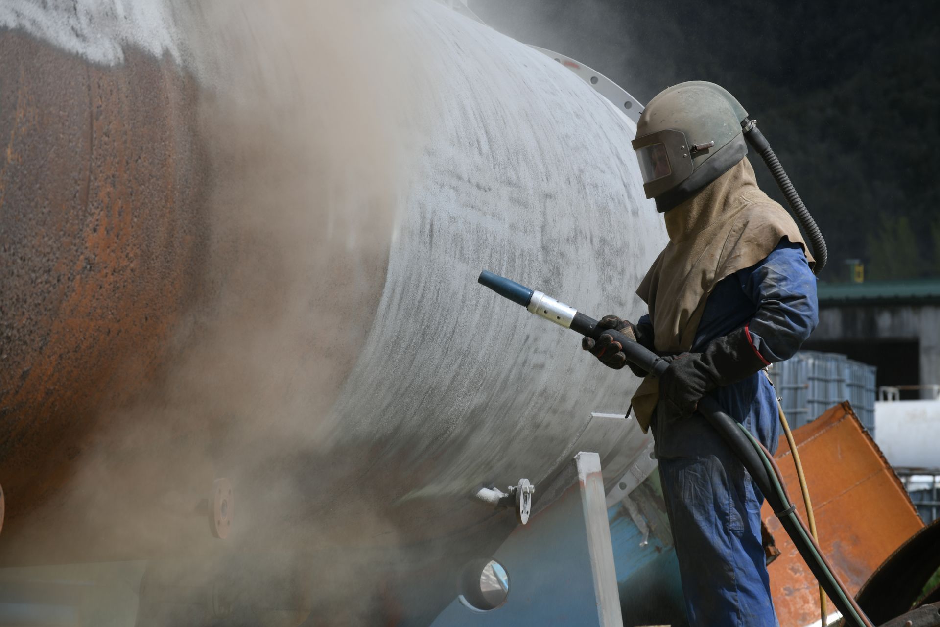 An engineer uses abrasive material on a steel casing while wearing protective gear. An engineer uses abrasive material on a steel casing while wearing protective gear.