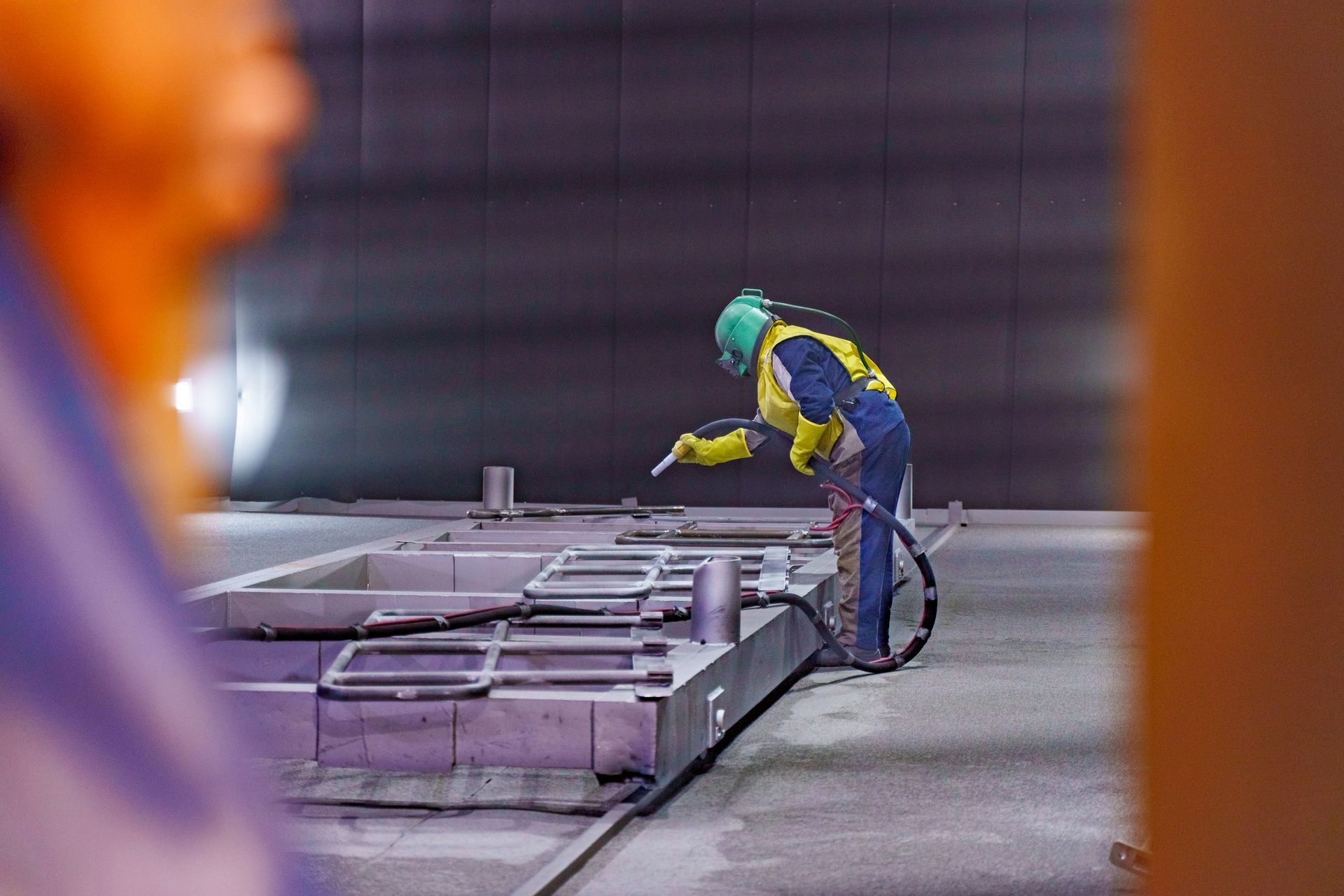 Worker in protective gear inspecting industrial equipment in a factory setting.