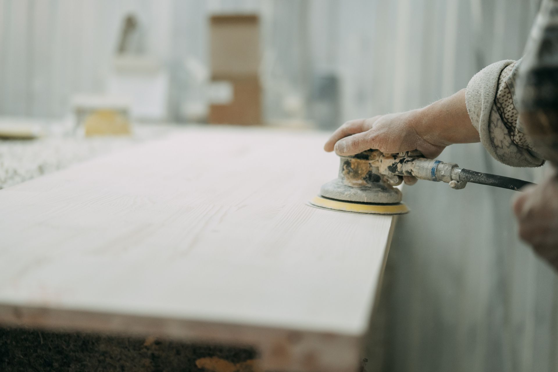 Carpenter is using an orbital sander to smooth a wooden plank in a workshop. Carpenter is using an orbital sander to smooth a wooden plank in a workshop.