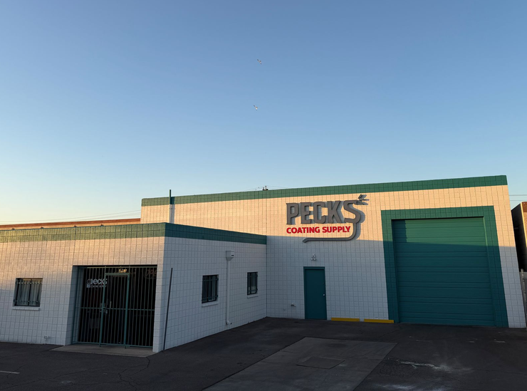 Small tan building with green garage doors and a parking lot under a clear blue sky