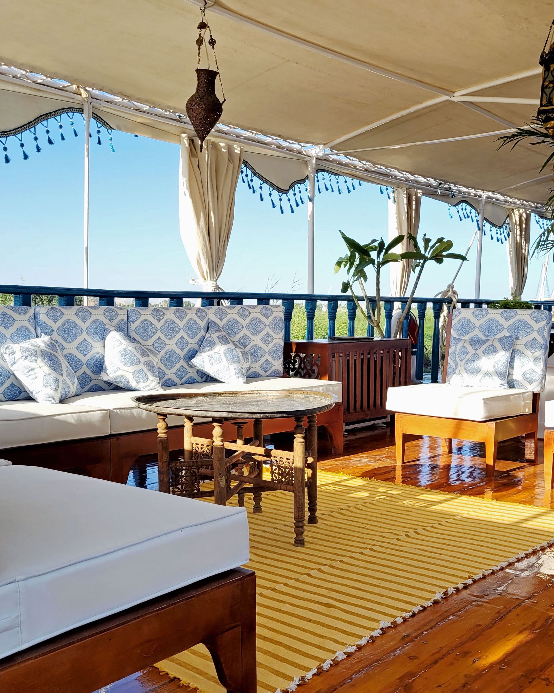 A photo of a cozy seating area on the deck of a traditional Egyptian sailing boat, the Dahabiya Kingfisher, which offers private cruises along the Nile river between Luxor and Aswan.