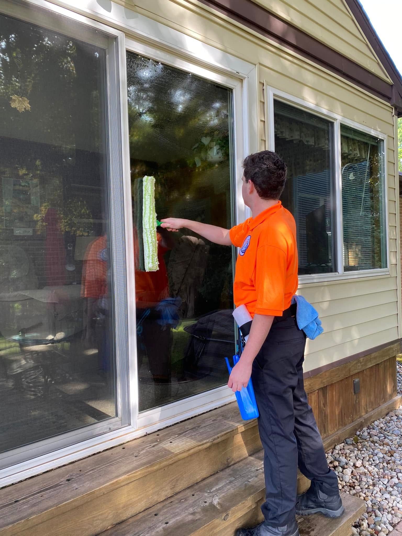 Person in orange shirt cleaning a glass sliding door with a squeegee outside a house