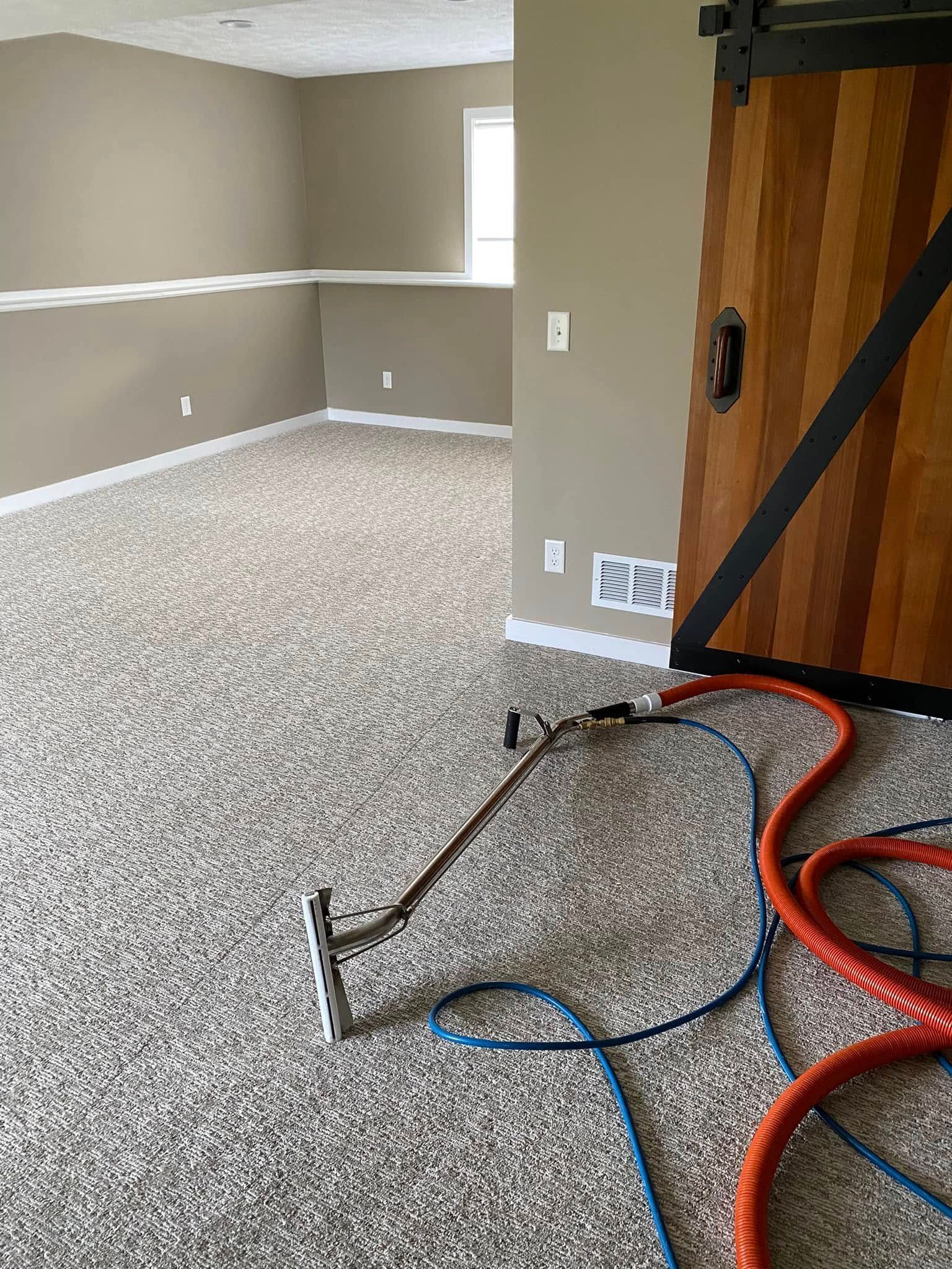Carpeted room with beige walls, a wooden door, and cleaning hoses on the floor.
